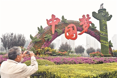 2013年9月30日,一名行人在北京复兴门桥拍摄“中国梦”主题花坛。(资料图片)