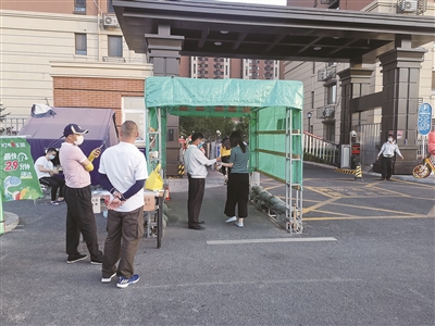 6月15日,在北京市丰台区花乡某小区门口,社区工作人员正按照要求检查居民出入证,并测量体温。 本报记者 喻大伟 摄