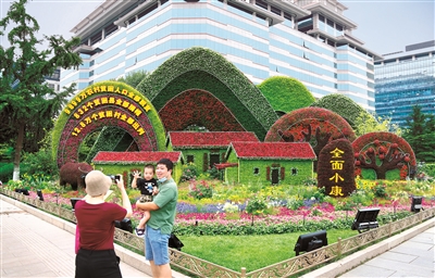 2021年6月,庆祝中国共产党成立100周年主题花坛亮相长安街沿线,西单东南角的全面小康主题花坛吸引市民驻足留影。 (图片来源:人民视觉)