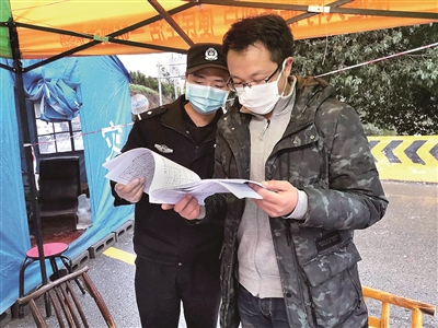 图为疫情期间,谢睿(右)在咸丰县清坪镇把界村大河边交通卡点查看车辆出入登记台账。 (湖北省咸丰县纪委监委供图)